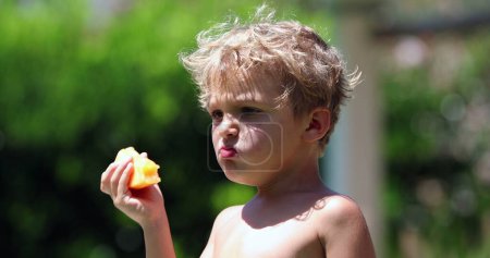 Foto de Niño olfateando afuera mientras mastica fruta - Imagen libre de derechos