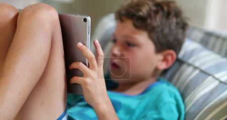 Téléchargez les photos : Enfant jouant jeu sur tablette. Jeune garçon hypnotisé par le jeu vidéo - en image libre de droit