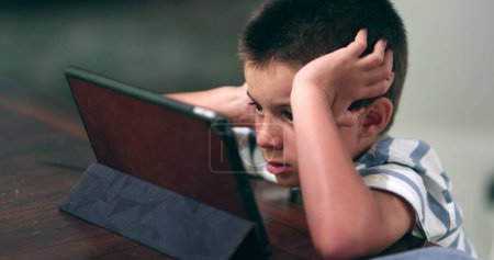 Photo for Young boy absorbed watching tablet content online. Kid watches film - Royalty Free Image