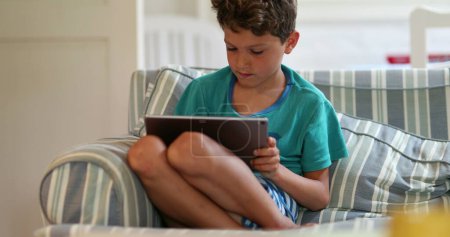 Photo for Candid child using tablet device on sofa. Kid browsing internet on tech device - Royalty Free Image