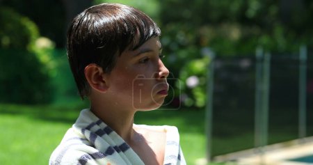 Téléchargez les photos : Enfant garçon mâchant de la nourriture enveloppée avec une serviette après la piscine pendant la journée d'été - en image libre de droit