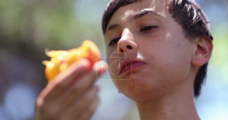 Téléchargez les photos : Enfant manger des fruits de pêche à l'extérieur en prenant une bouchée de collation saine - en image libre de droit