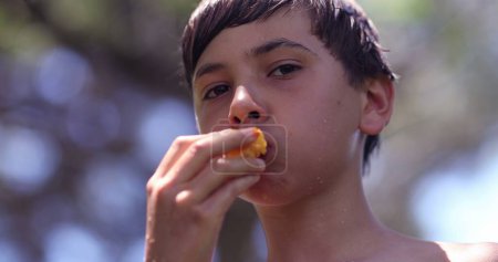 Foto de Niño pensativo comiendo fruta al aire libre. Niño reflexivo masticando melocotón - Imagen libre de derechos