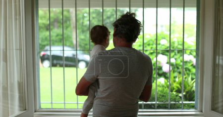 Photo for Baby and grandfather next to window during rainy day - Royalty Free Image