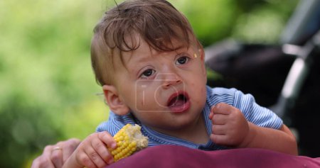 Téléchargez les photos : Bébé bébé mignon mangeant du maïs. Pensive enfant en bas âge garçon penser tout en grignotant - en image libre de droit