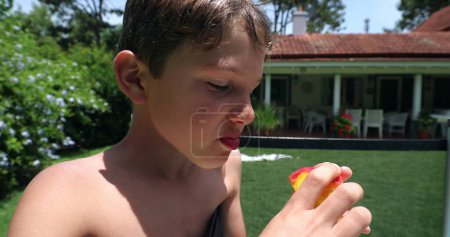 Photo for Child eating peach fruit outdoors. Young boy eats healthy snack outside during summer day - Royalty Free Image