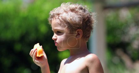 Photo for Handsome toddler child holding and eating yellow melon fruit - Royalty Free Image