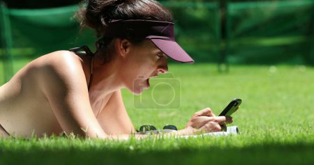 Foto de Mujer usando el teléfono celular fuera acostado en la hierba al aire libre - Imagen libre de derechos
