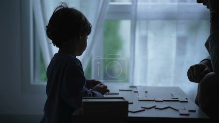 Photo for Mother hanging out with son at home in silhouette by window. Mom homeschooling child at home playing board game - Royalty Free Image