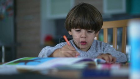 Téléchargez les photos : Un petit garçon concentré dessin à la maison. Mode de vie créatif de l'enfance. Candid kid faire une activité d'éducation à domicile - en image libre de droit