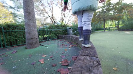 Foto de Niños pies de primer plano con botas equilibrio de entrenamiento en la superficie de madera del patio. Desarrollo infantil despreocupado concepto de estilo de vida - Imagen libre de derechos
