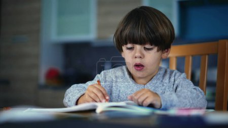 Photo for One small boy drawing at home. Child doing school work indoors holding pen on paper - Royalty Free Image