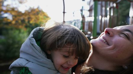 Téléchargez les photos : Mère et enfant heureux faisant eskimo baiser avec le nez debout à l'extérieur avec éclat de la lumière du soleil. Concept de mode de vie maternel - en image libre de droit