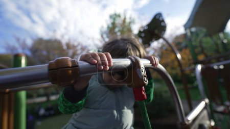Téléchargez les photos : Petit enfant actif tenant dans la barre de métal à l'aire de jeux à l'extérieur pendant la saison d'automne. Exercices pour enfants à l'extérieur mains rapprochées - en image libre de droit