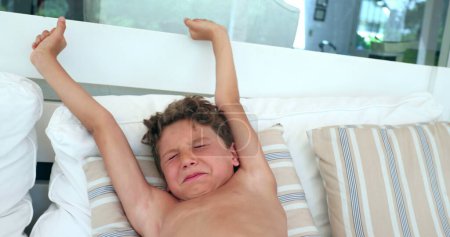 Téléchargez les photos : Enfant étirant le corps, jeune garçon endormi mignon se réveillant de la sieste étire le corps, se sentant frais et reposant - en image libre de droit