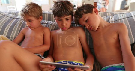 Téléchargez les photos : Enfants devant tablette sur le canapé de la maison. Enfants frères et sœurs hypnotisés par écran, regardant un film ou un contenu - en image libre de droit