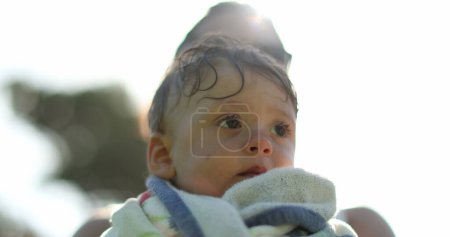 Photo for Infant toddler wrapped in towel after pool held by parent in sunlight lens-flare - Royalty Free Image