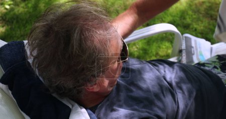 Téléchargez les photos : Homme plus âgé se détendre dehors couché dans la nature. Personne âgée se reposant sur le point de faire une sieste - en image libre de droit