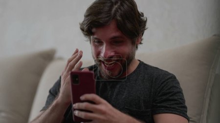 Photo for Happy man reacting positively to news notification on cellphone device while sitting at home couch. Ecstatic person celebrating success - Royalty Free Image
