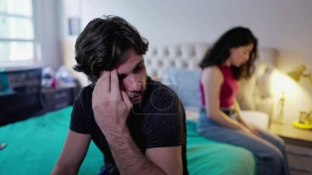 Photo for Sad couple with problems at home sitting on bed. Man and woman looking down feeling despair and sadness. Hopeless marriage dysfunction - Royalty Free Image