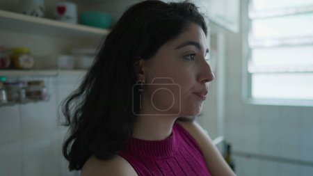 Photo for Contemplative young woman closeup profile face in deep thought. Pensive female person in 30s thinking about decision while standing at kitchen - Royalty Free Image