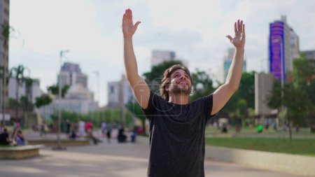 Téléchargez les photos : Jeune homme exultant exprimant espoir et foi avec les bras levés célébrant le triomphe en plein air dans le parc - en image libre de droit