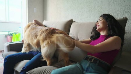 Téléchargez les photos : Joyeux couple avec leur chien assis sur le canapé. Récupérateur d'or ludique interagissant avec l'homme et la femme. Concept de bonheur des propriétaires d'animaux de compagnie - en image libre de droit