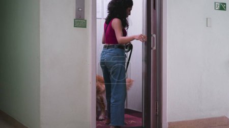 Téléchargez les photos : Femme ouvrant la porte de l'ascenseur allant se promener avec son chien en laisse. routine quotidienne de la personne style de vie domestique entrant ascenseur avec animal de compagnie - en image libre de droit