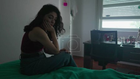 Photo for One pensive preoccupied young woman sits by bedside with contemplative expression. Female person in 30s struggling with inner emotions - Royalty Free Image
