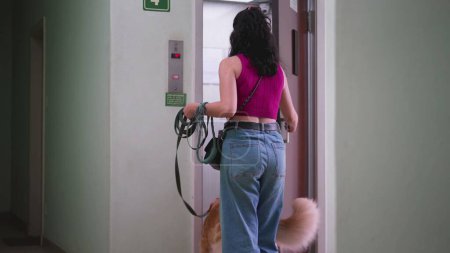 Téléchargez les photos : Femme ouvrant la porte de l'ascenseur allant se promener avec son chien en laisse. routine quotidienne de la personne style de vie domestique entrant ascenseur avec animal de compagnie - en image libre de droit