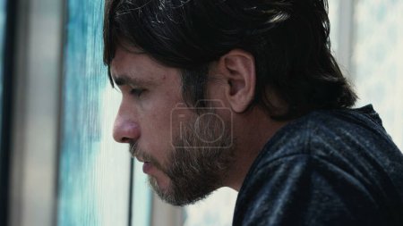 Photo for Young man feeling regret leaning on window feeling despair. Hopeless male person in 30s feeling solitude and desperation - Royalty Free Image