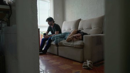 Photo for Young Couple in relationship turmoil. Man and woman in conflict not making eye contact with each other. Female partner lying on couch ignoring boyfriend - Royalty Free Image