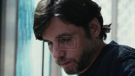 Photo for Close-up of Depressed Young Man Leaning on Window at Home, Feeling Worried and Anxious. Portrait of a Person Suffering from Mental Pain and Emotional Turmoil - Royalty Free Image