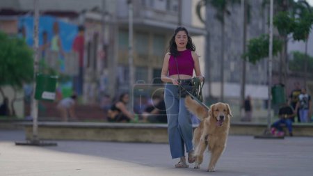 Téléchargez les photos : Femme marchant en ville avec son chien en laisse. Mode de vie quotidien de la personne qui va se promener avec son Golden Retriever Pet - en image libre de droit