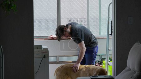Photo for Young man petting his Dog at home apartment by window. Candid male person with his Golden Retriever Pet indoors - Royalty Free Image