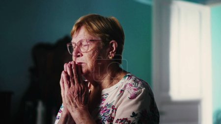Photo for Religious older woman Praying to God in bedroom. Hopeful Elderly Mature Lady in Prayer feeling connected to a higher power, devoted older person - Royalty Free Image