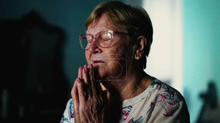 Foto de Fiel anciana rezando en casa con los ojos cerrados. Tema espiritual esperanzador durante la vejez - Imagen libre de derechos
