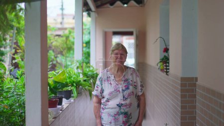 Téléchargez les photos : Femme âgée debout à la maison dans la cour arrière de la résidence sud-américaine casua. Senior femme dans les années 70, domestique authentiques vraies personnes - en image libre de droit