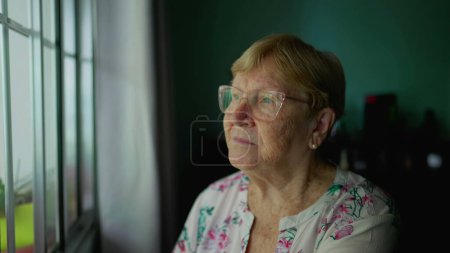 Téléchargez les photos : Gros plan sur le visage d'une femme âgée pensive contemplant la vie, expression réfléchie alors qu'elle regarde la fenêtre de la maison isolée - en image libre de droit