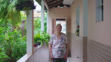 Téléchargez les photos : Femme âgée debout à la maison dans la cour arrière de la résidence sud-américaine casua. Senior femme dans les années 70, domestique authentiques vraies personnes - en image libre de droit