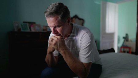 Photo for Pensive older man sitting by bedside in deep contemplation. Middle-aged person pondering problem with hand in chin thinking - Royalty Free Image