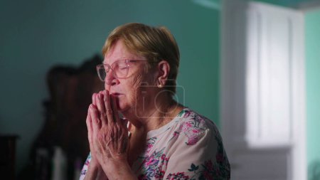Téléchargez les photos : Femme âgée religieuse pleine d'espoir priant Dieu dans la chambre à coucher, se sentant connectée à une puissance supérieure et dévouée dans la prière - en image libre de droit