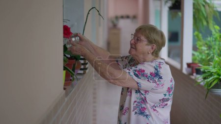 Foto de Candid Daily Routine of Elderly Woman Planta de riego con botella de agua en el patio trasero del hogar, exhibiendo un estilo de vida genuino para personas mayores - Imagen libre de derechos
