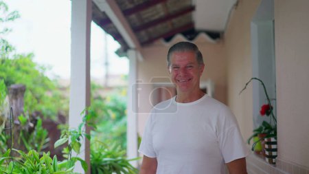 Téléchargez les photos : Joyeux homme à la retraite souriant à la caméra dans la cour arrière de la maison, plan rapproché pistage - en image libre de droit