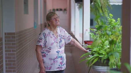 Téléchargez les photos : Femme âgée réfléchie debout dehors à la maison arrière-cour se souvenant des souvenirs passés. 80 ans personne en contemplation - en image libre de droit
