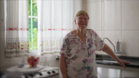 Photo for Senior woman standing in kitchen by window. One elderly caucasian 80s person looking at camera. authentic real life domestic scene - Royalty Free Image