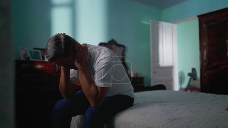 Foto de Hombre deprimido sentado junto a la cama en el dormitorio. Triste persona infeliz mirando hacia abajo sufriendo de enfermedad mental - Imagen libre de derechos