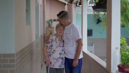 Foto de Hijo adulto besando a la madre mayor en la frente mientras posan juntos, cuidado de ancianos con el brazo alrededor de los padres ancianos - Imagen libre de derechos