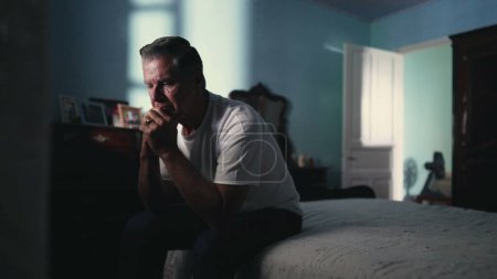 Photo for Contemplative older man sitting by bed pondering problems. Person in 50s dwelling with life_s difficulties. Loneliness and solitude concept in middle age suffering from abandonment - Royalty Free Image