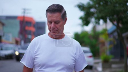 Photo for Pensive senior man walking in street in daylight. A middle-age caucasian male strolling in urban environment with thoughtful expression, contemplative emotion - Royalty Free Image